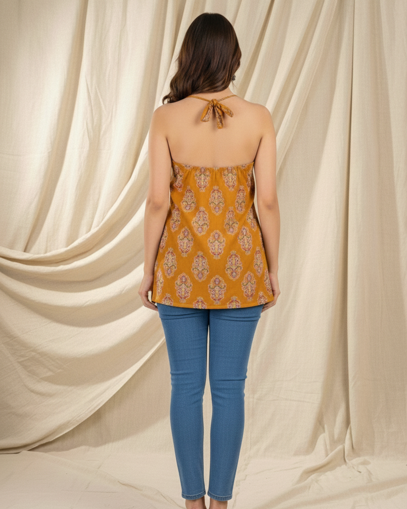 Woman wearing a mustard yellow top with floral patterns and blue jeans against a beige curtain background