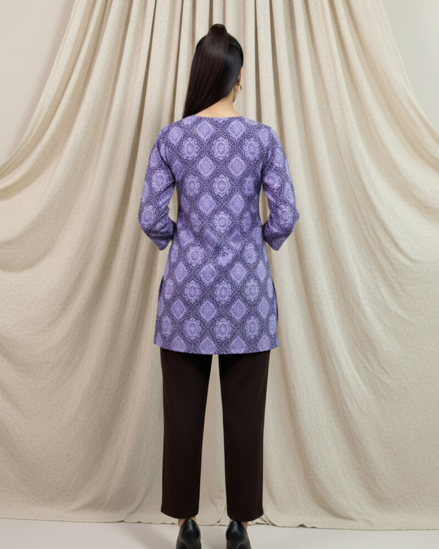Person wearing a purple patterned top and black pants against a beige curtain backdrop