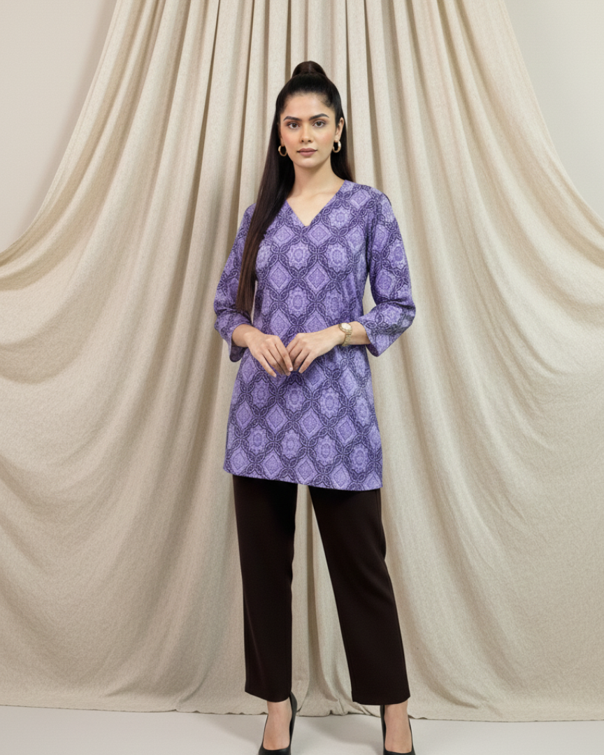 Woman wearing a purple patterned top and black pants against a beige curtain background