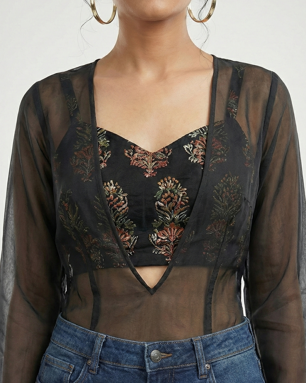 Person wearing a sheer top with floral embroidery and high-waisted jeans on a white background