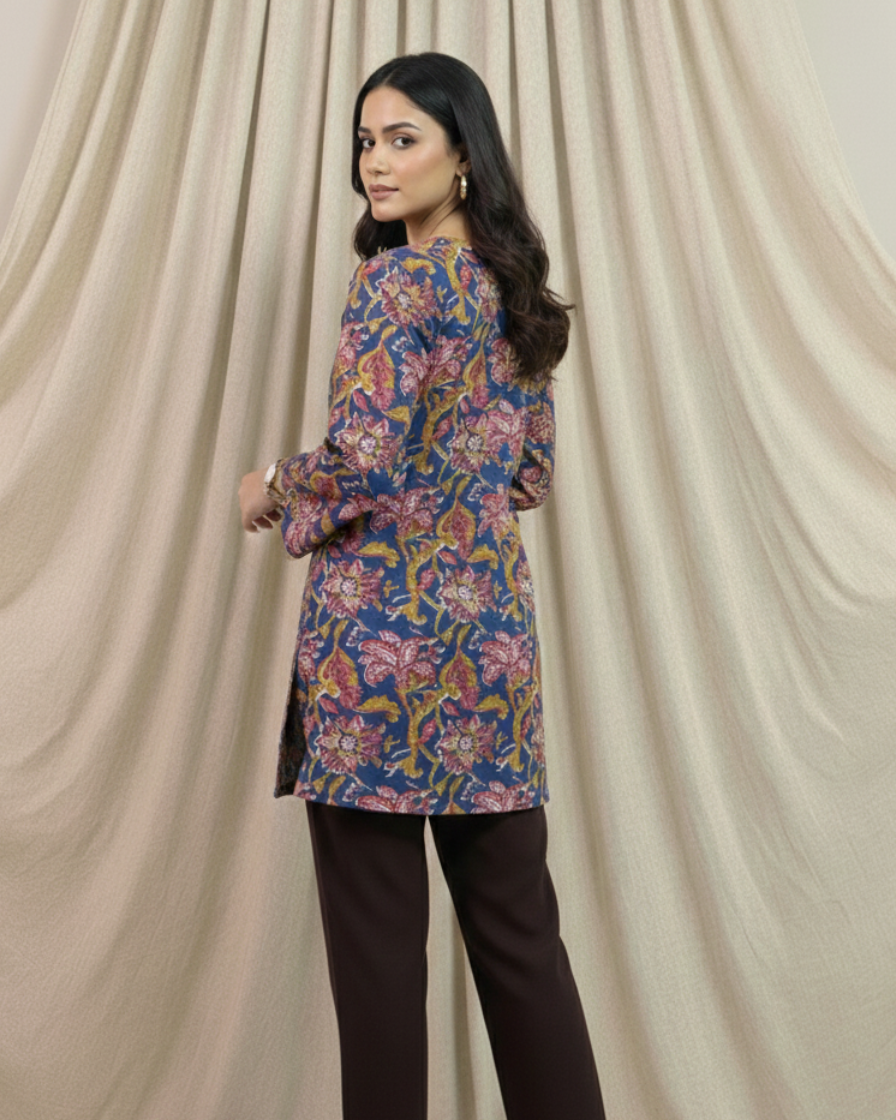 Woman wearing a floral top and dark pants against a beige curtain backdrop