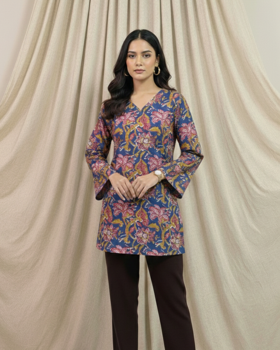 Woman wearing a floral top and black pants against a beige curtain background
