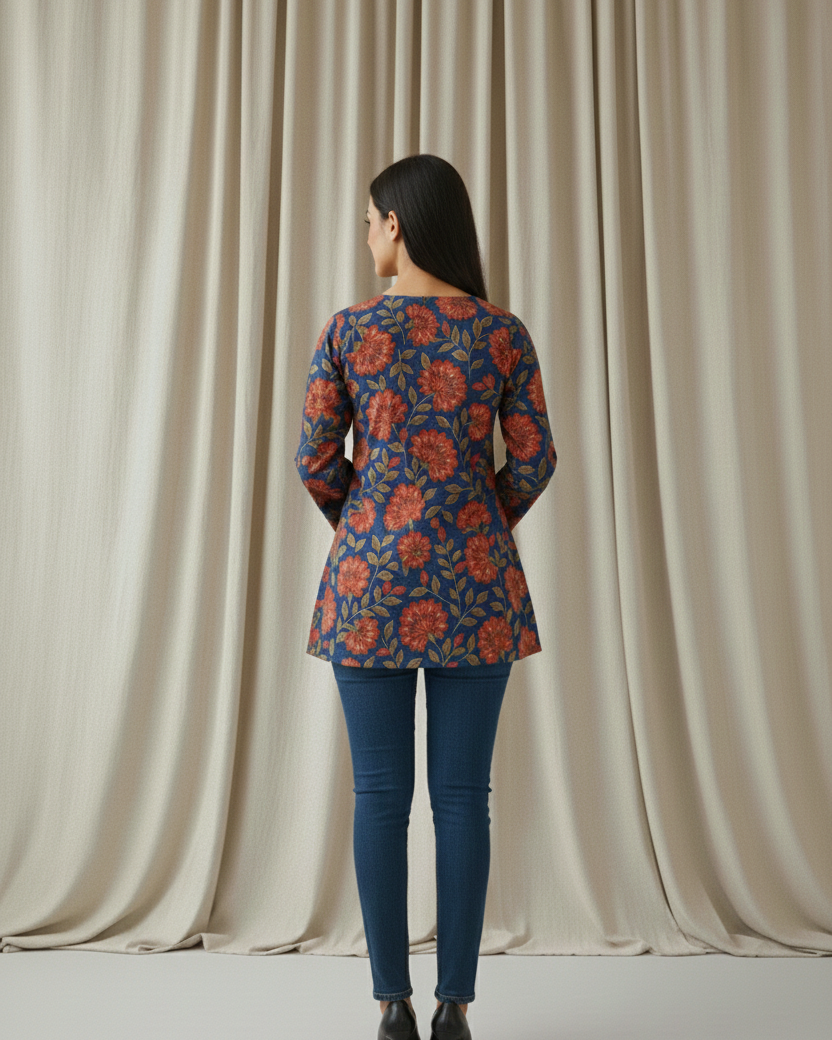 Woman wearing a floral patterned top and blue jeans standing in front of beige curtains.